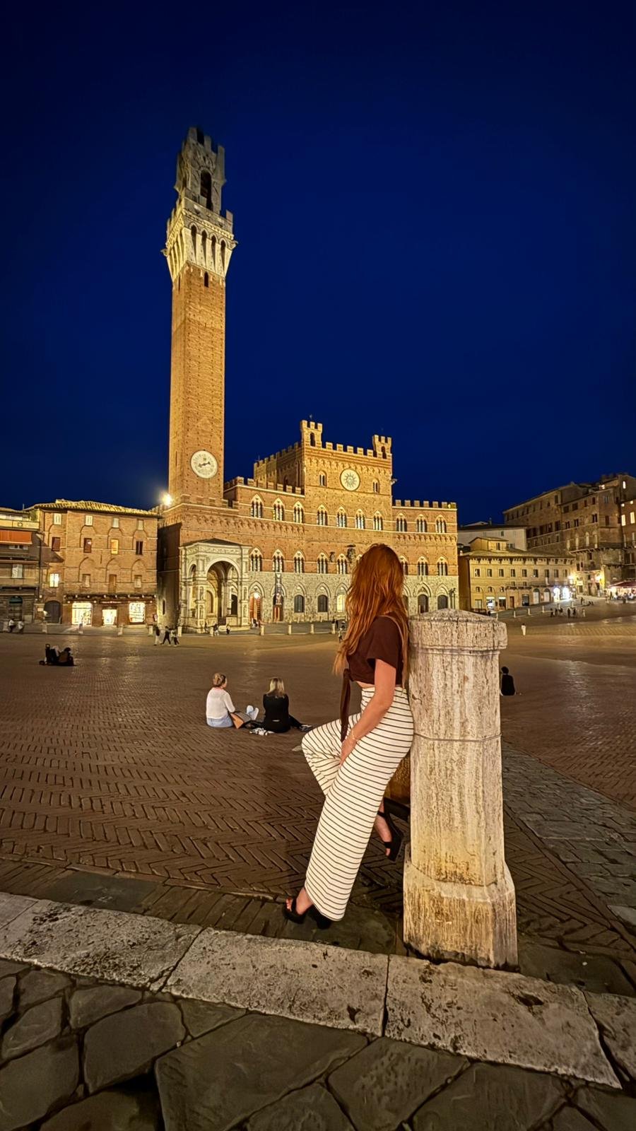 Kobieta o zmierzchu na tle wieży Torre del Mangia i Piazza del Campo w Sienie