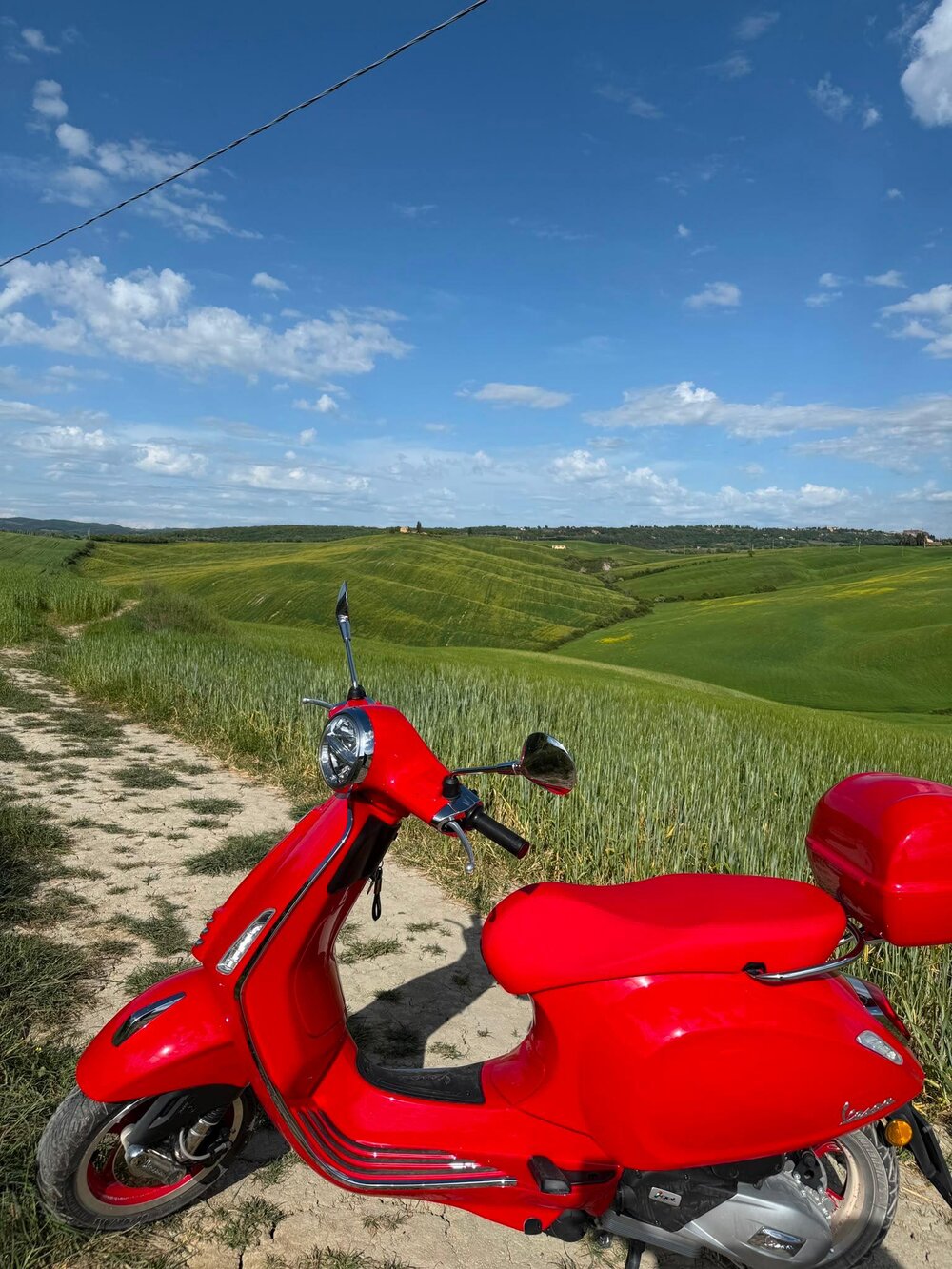 Czerwony skuter Vespa na tle zielonych toskańskich wzgórz